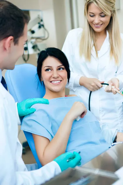 smiling woman in dental chair with dentist and hygienist next to her